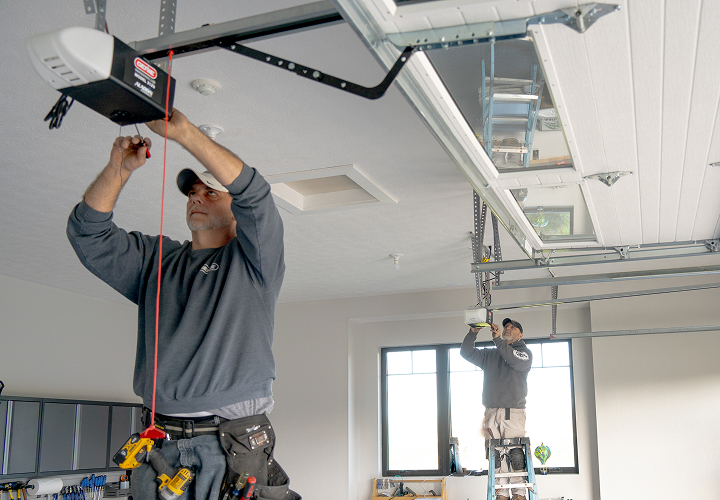 Two professional technicians installing a garage door opener overhead